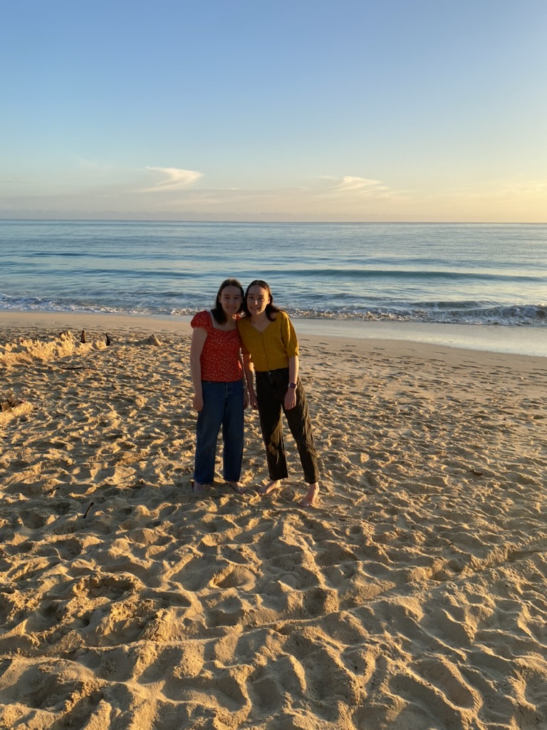 Two girls on the beach at sunrise with the water behind them.