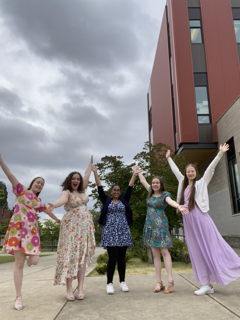 Five girls in dresses with their hands in the air.