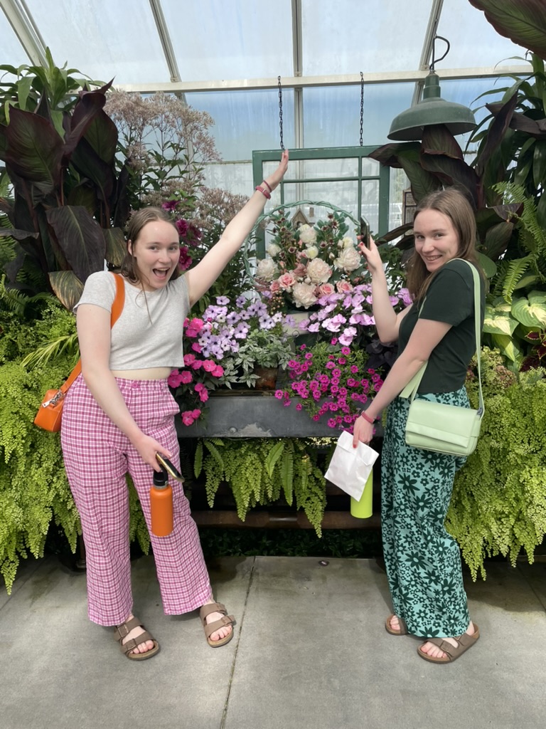 Two girls in a conservatory in front of lots of lush green plants.
