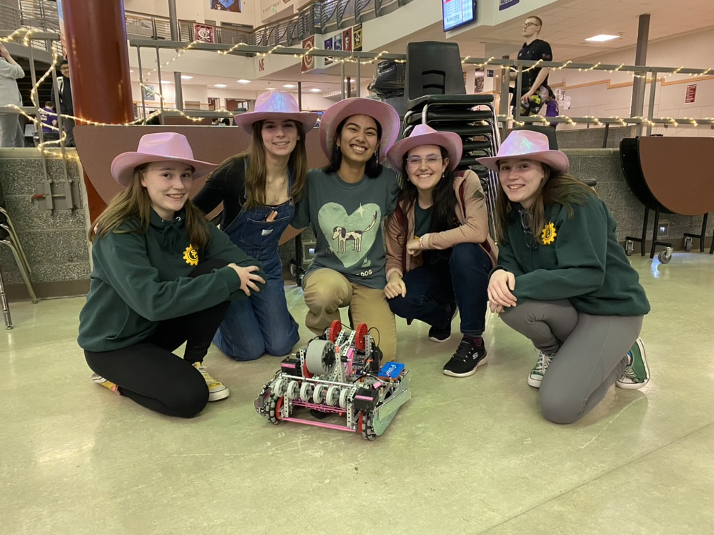 Five girls in pink cowboy hats crouched around a pink and purple robot.