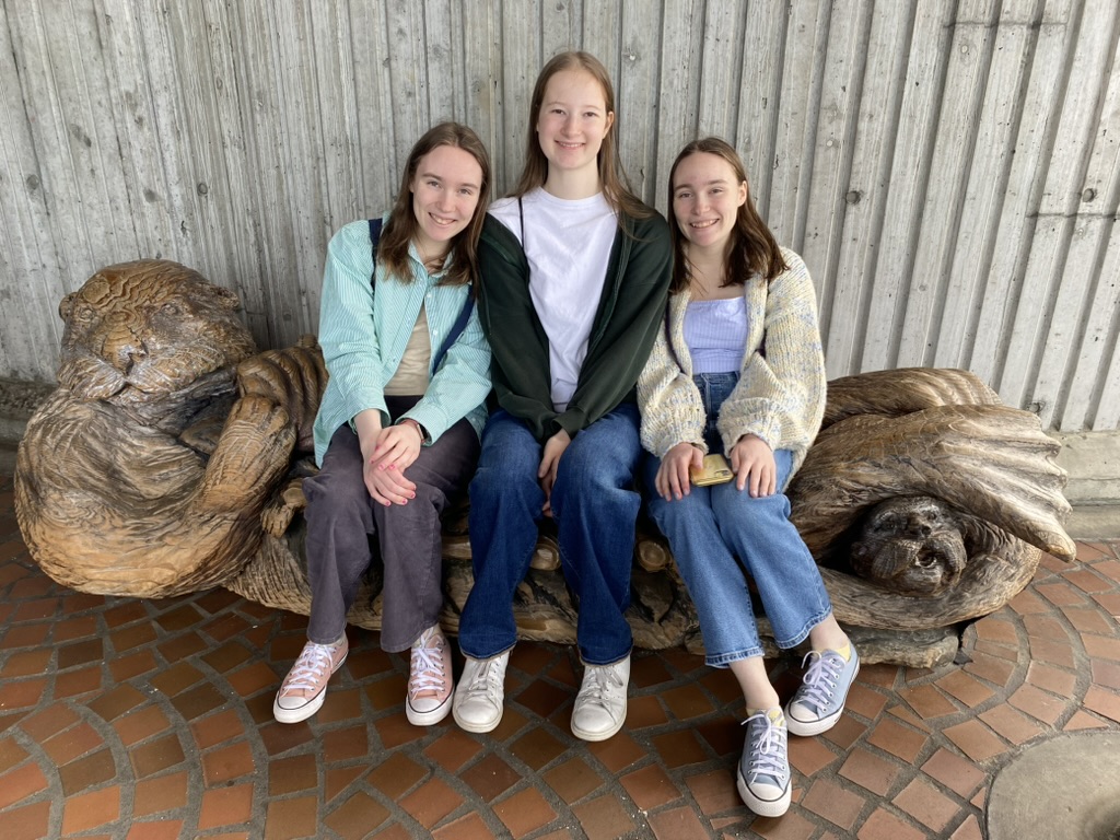 Three girls smiling on an otter bench.
