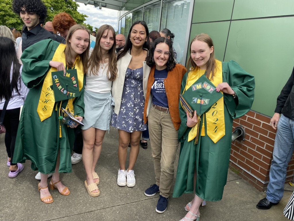 Five girls smiling, two are in graduation gowns holding their caps.