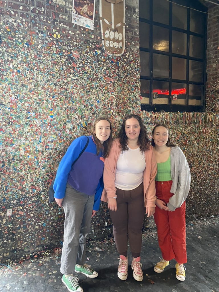Three girls standing in front of a gum wall.