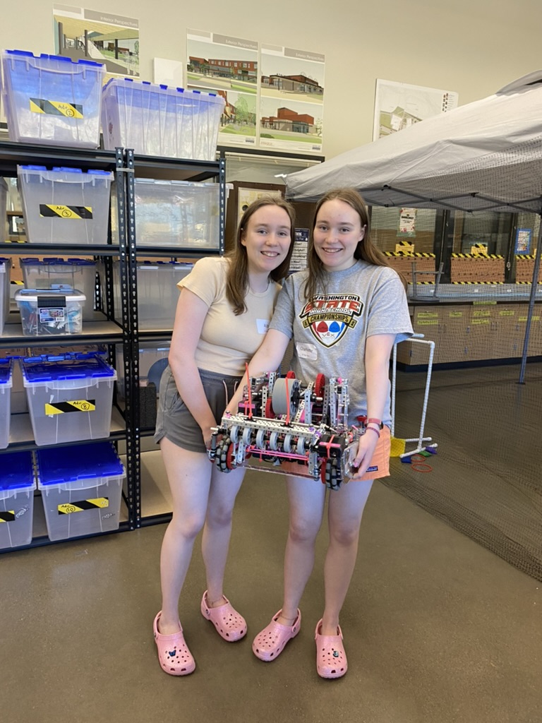 Two girls holding a pink and purple robot and smiling.
