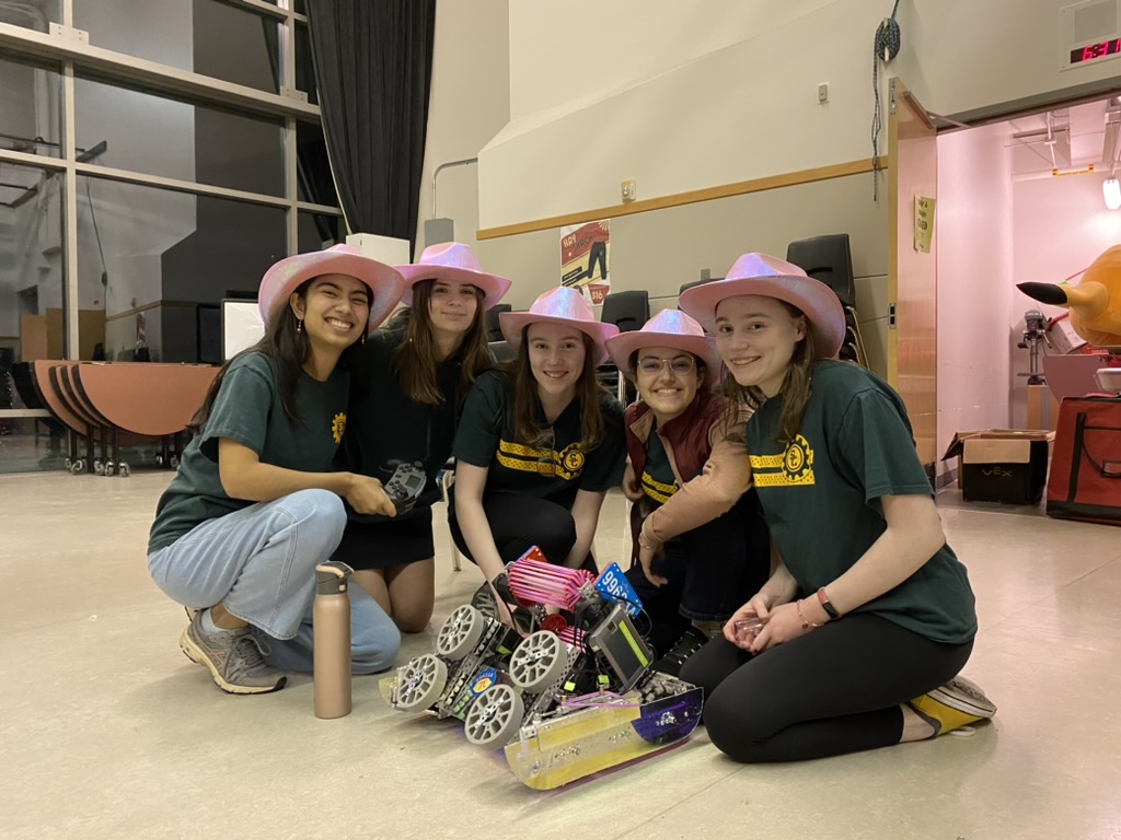 Five girls in pink cowboy hats kneeling around a pink and purple robot.