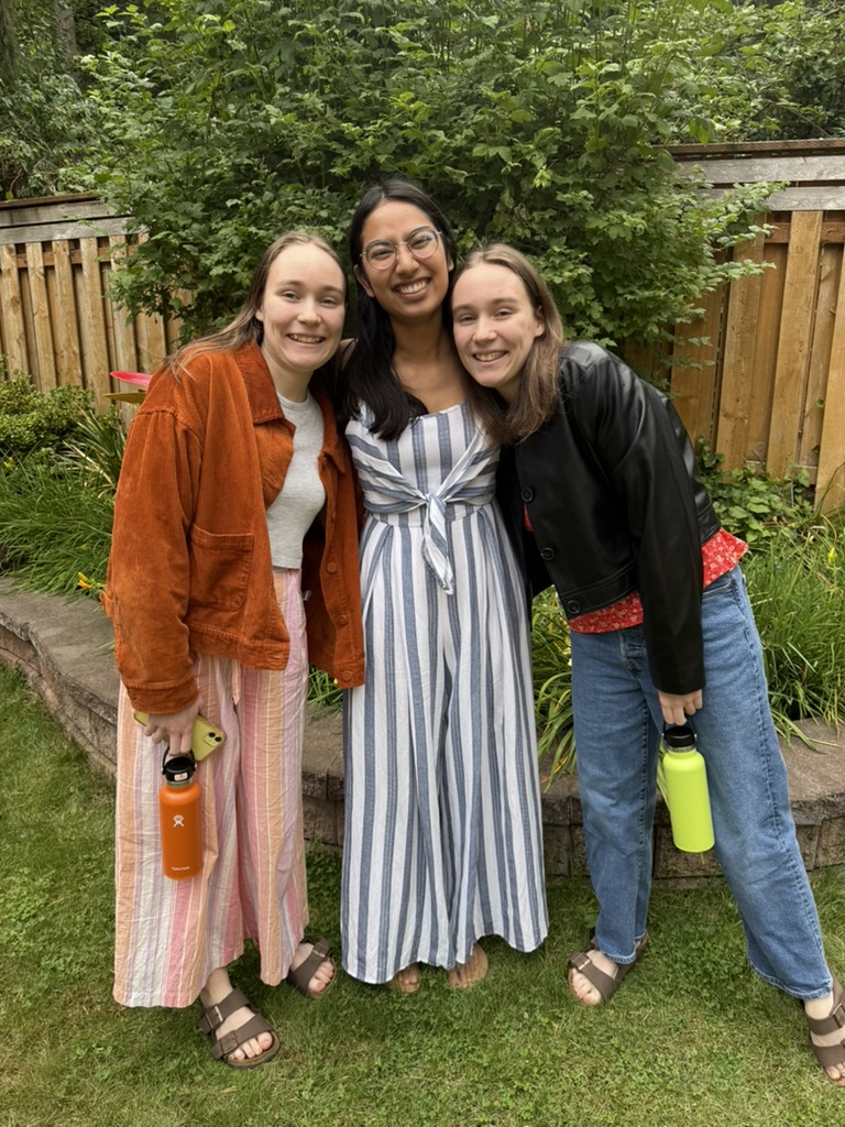 Three girls smiling in a garden with lots of green plants behind them.