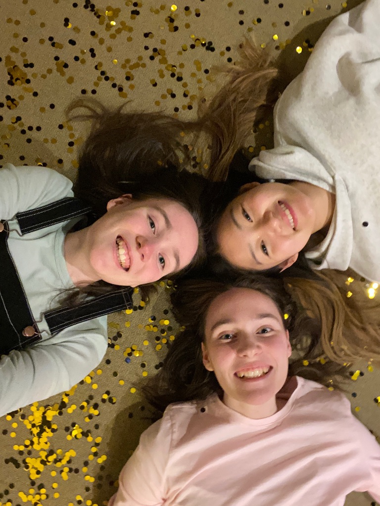 Three girls laying on the floor in black and gold confetti on New Year's Eve.
