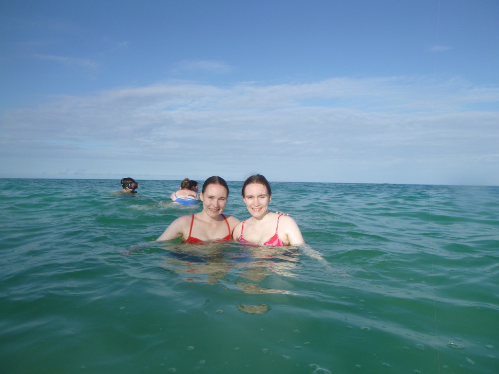 Two girls swimming in the ocean under a blue sky.