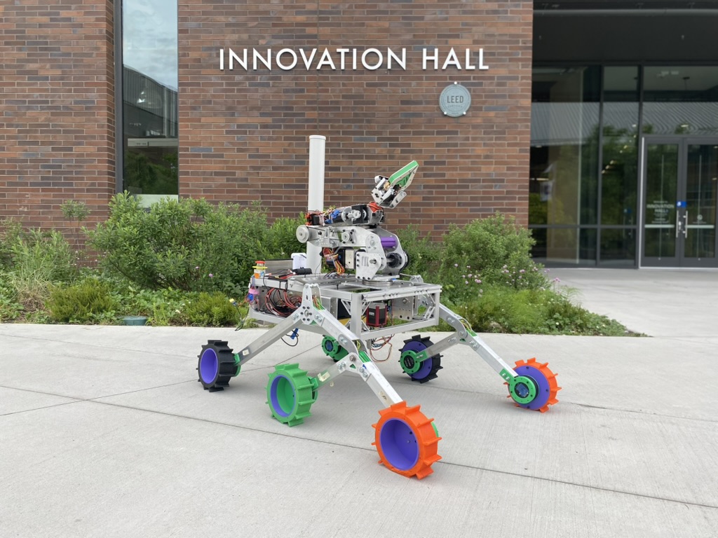 A gray rover with colorful wheels in front of a brick building.