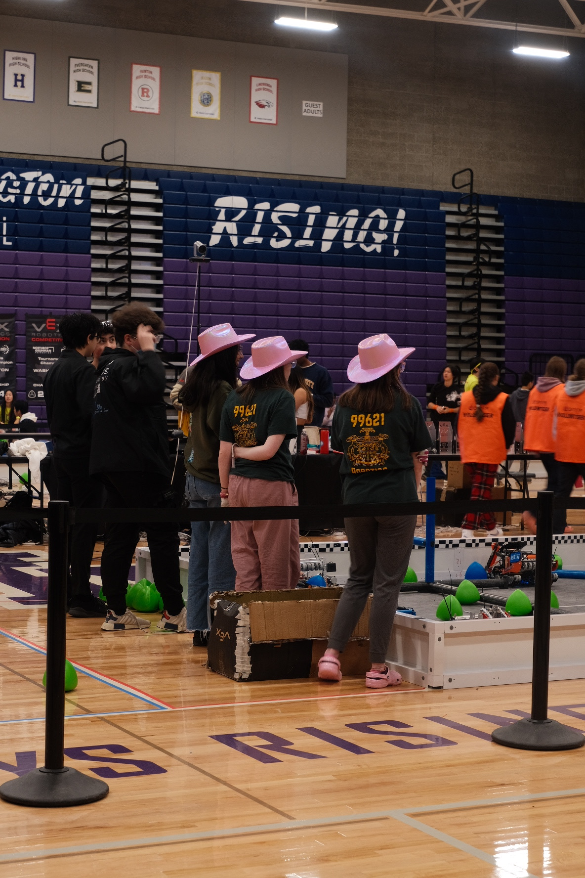 Three girls in pink cowboy hats face away from the camera, standing above a robot field.
