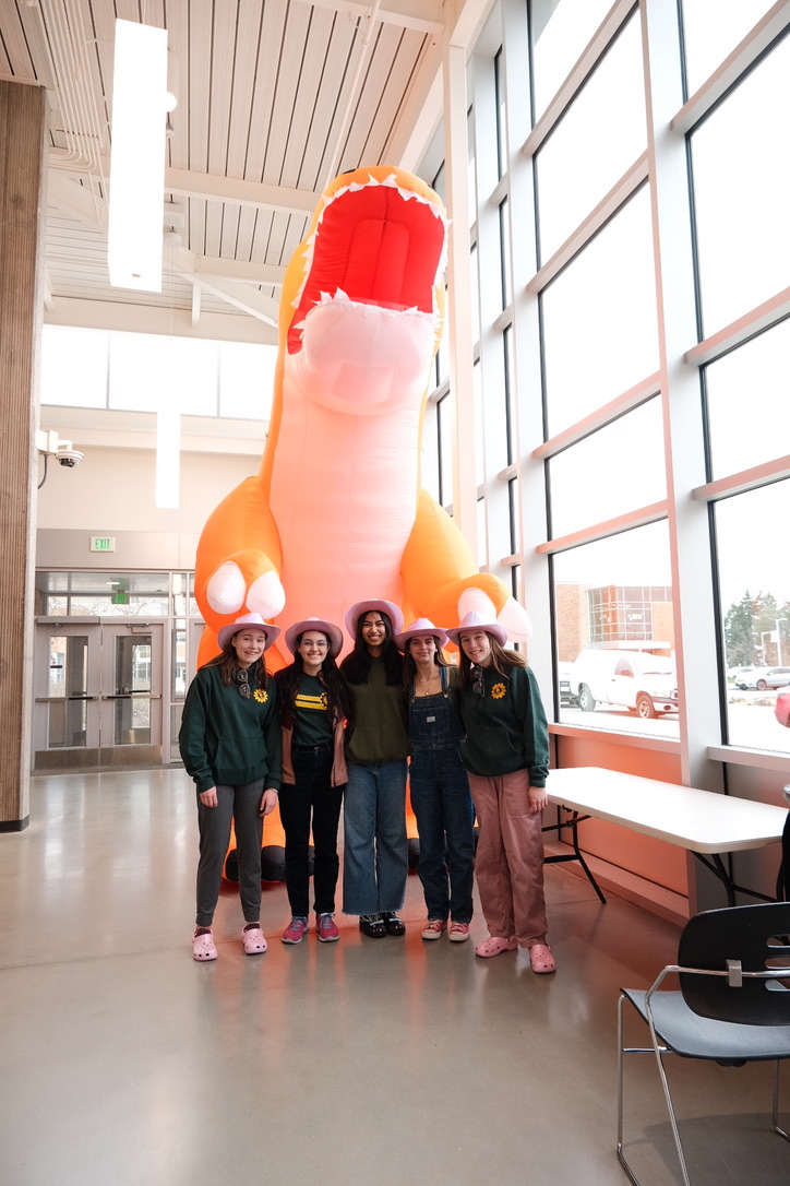 Five girls in pink cowboy hats in front of a giant orange inflatable dinosaur.