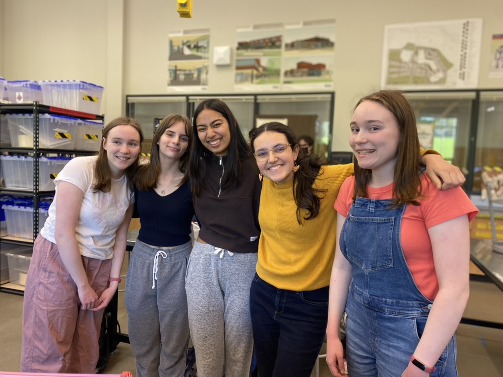 Five girls standing close together smiling.