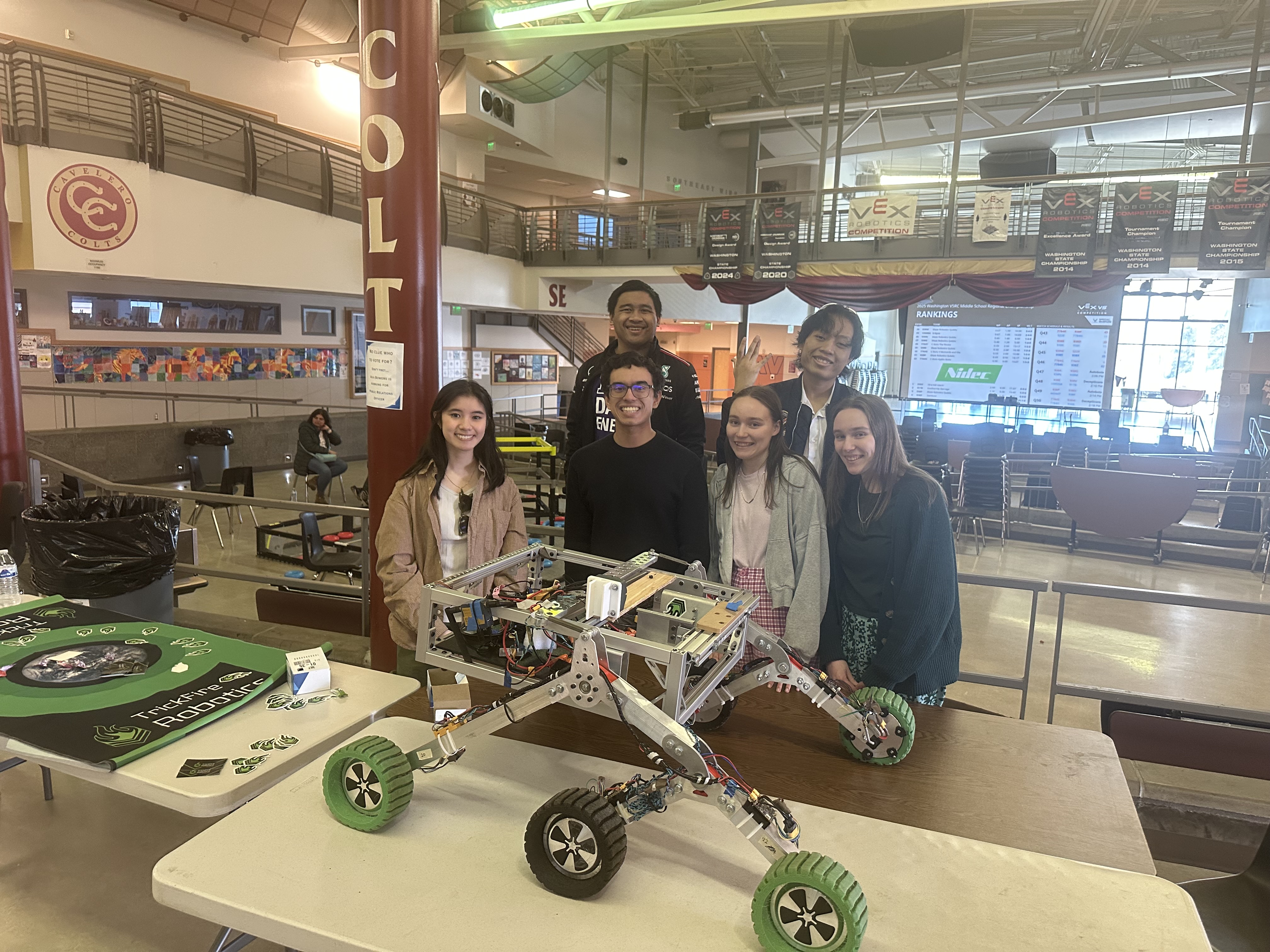 Six students smile behind a table with a gray rover.