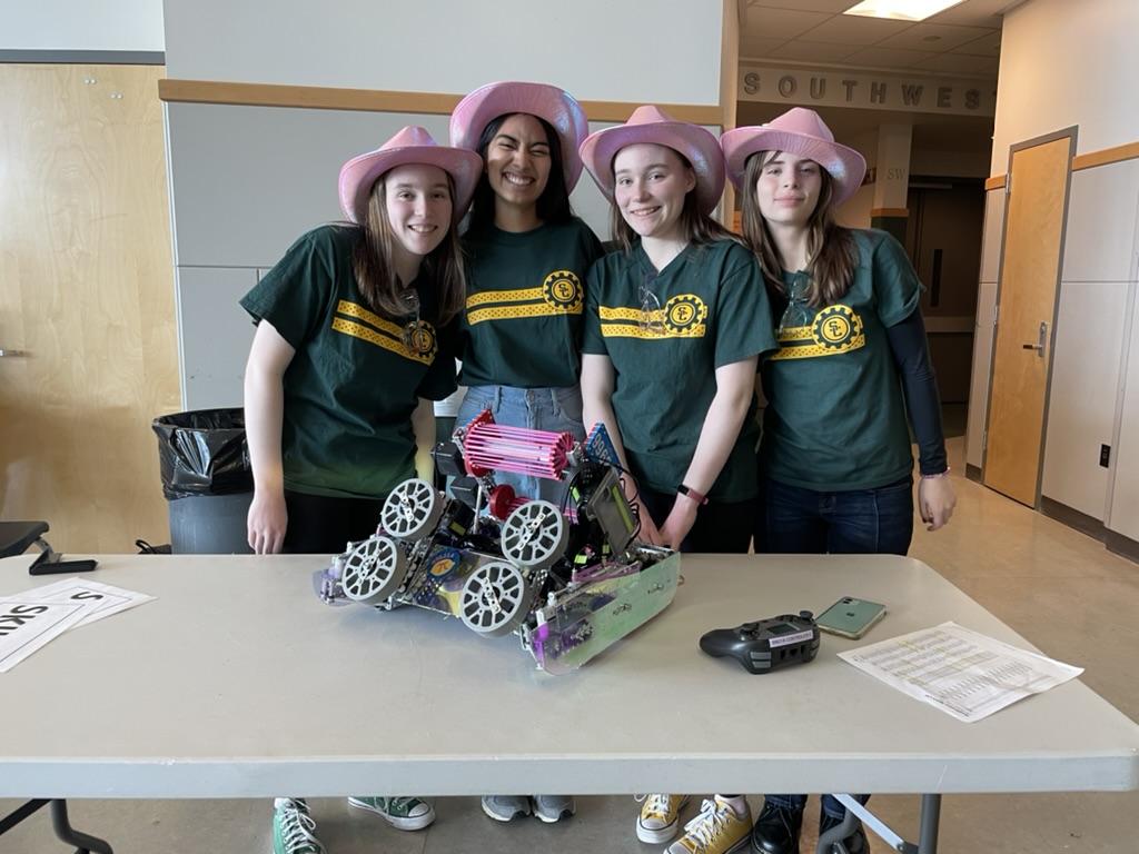 Four girls in pink cowboy hats standing behind a table with a pink and purple robot.