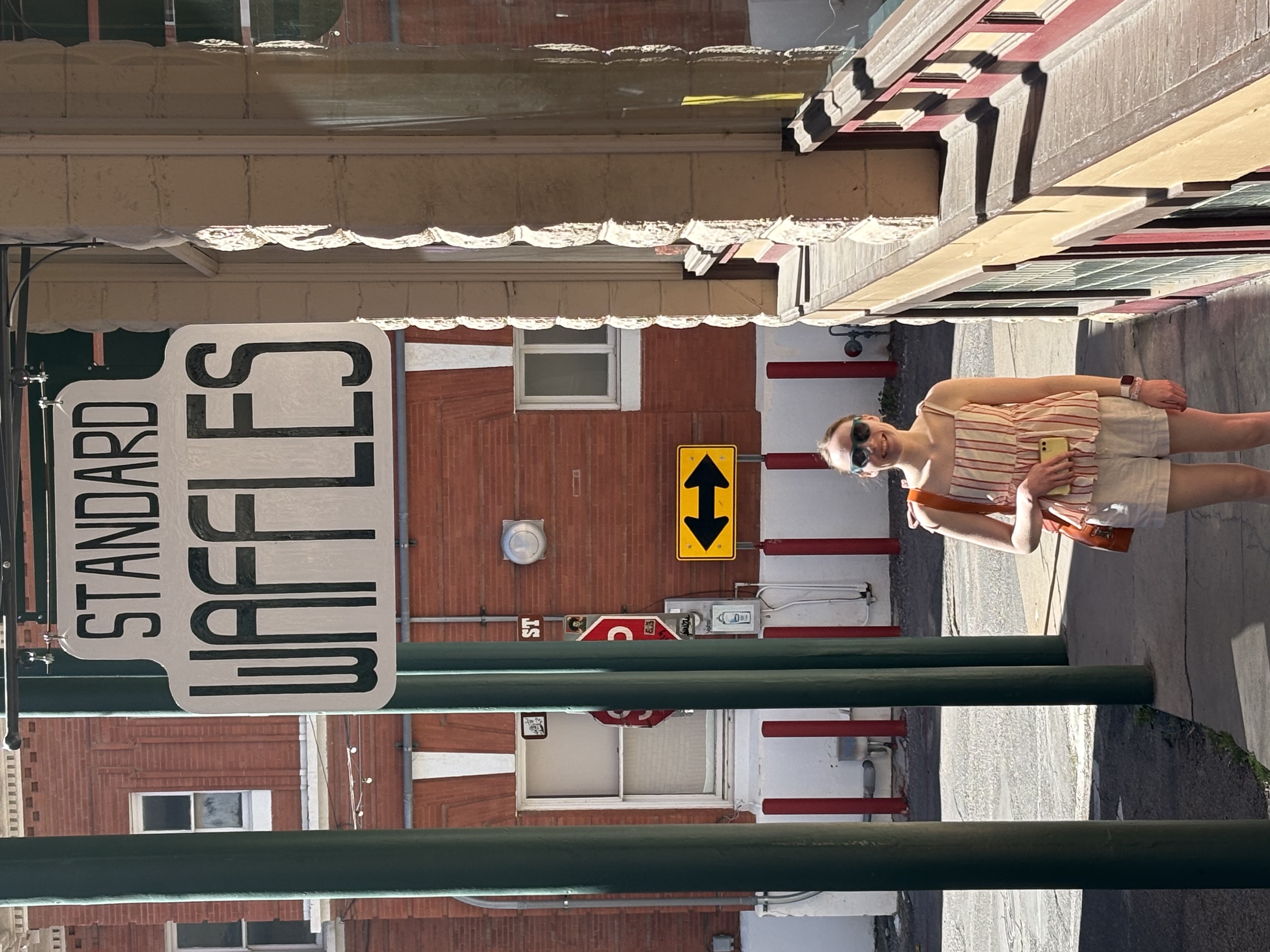 A girl in sunglasses standing under a sign that says WAFFLES.